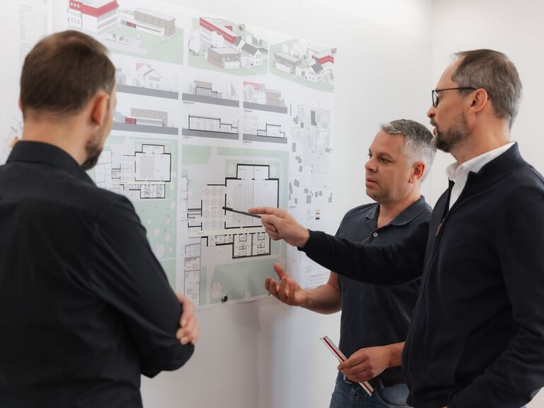 Drei Mitarbeiter besprechen eine Planwand