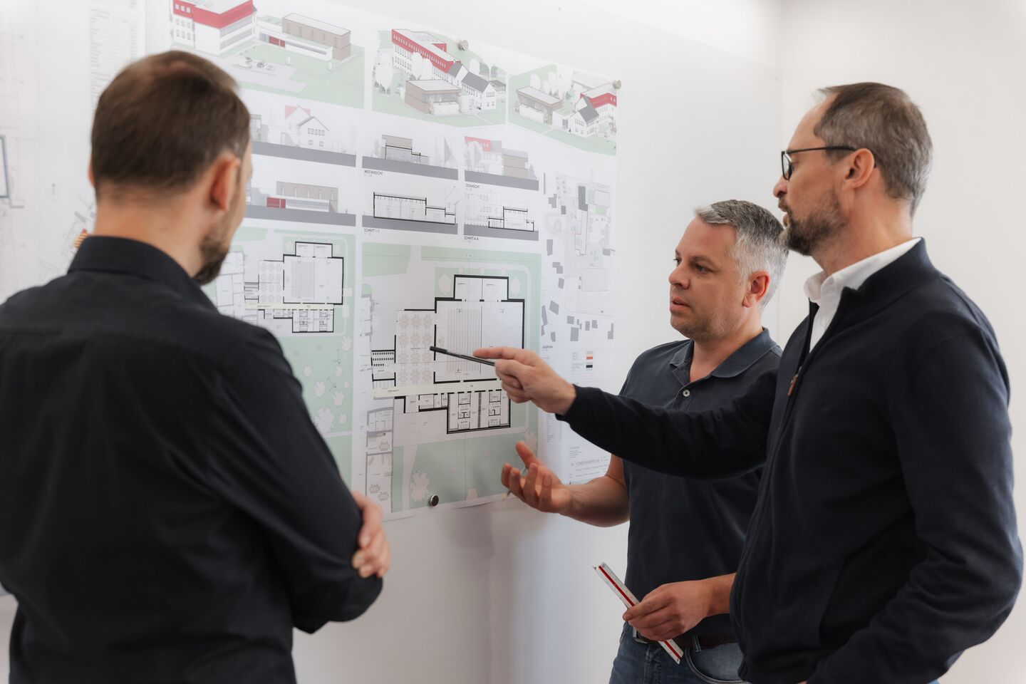 Drei Mitarbeiter besprechen eine Planwand
